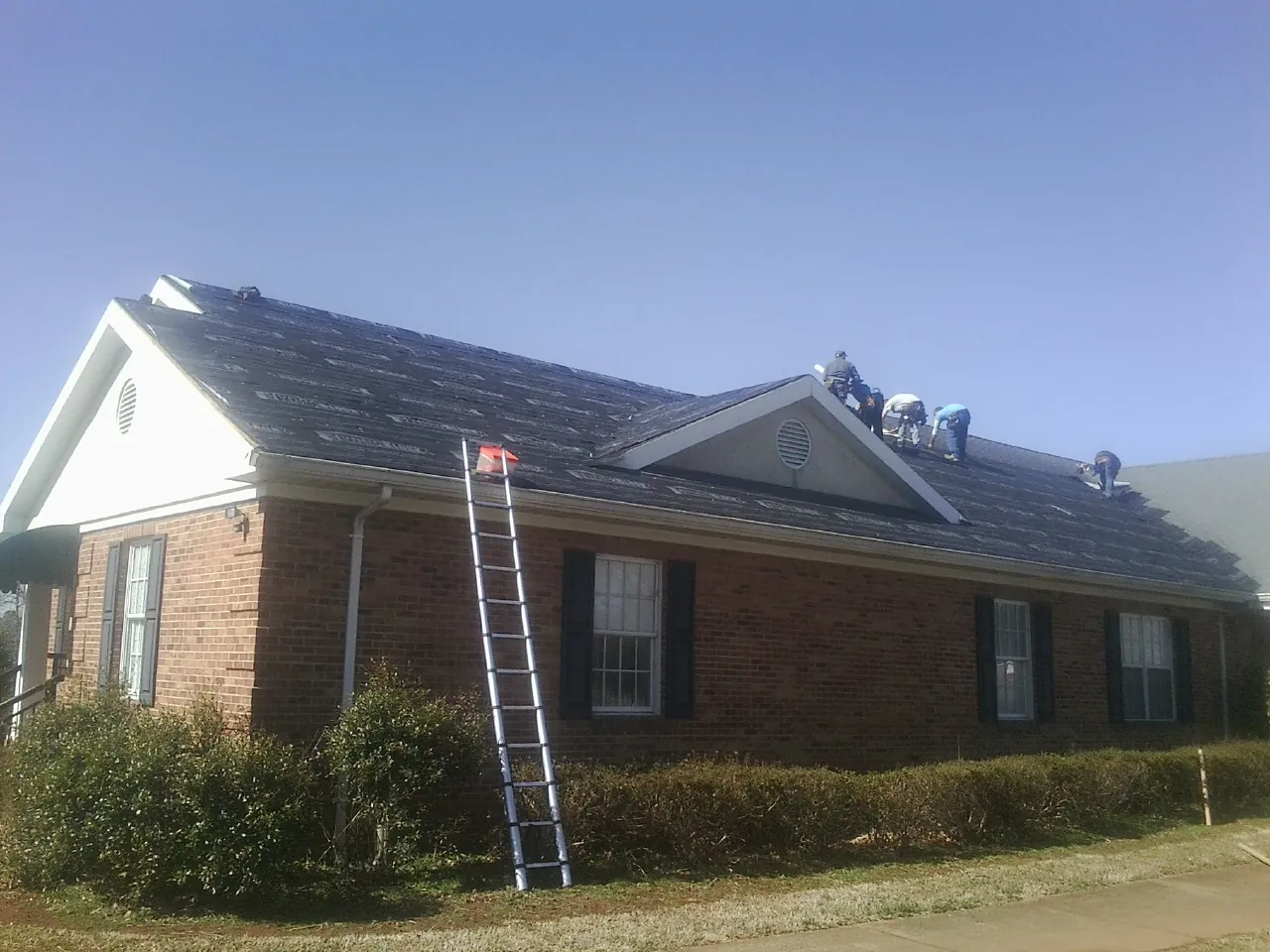 Crew tearing shingles off a brick ranch roof with a ladder set — Emergency Roof Repair work by our crew in Gambrills
