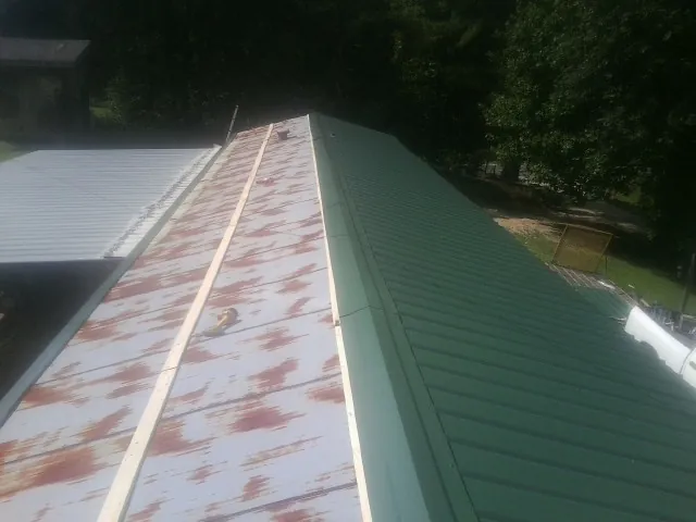 Old rusted panels beside newly installed green metal roofing — Wind Damage Roof Repair by Roofing Brothers in Gambrills