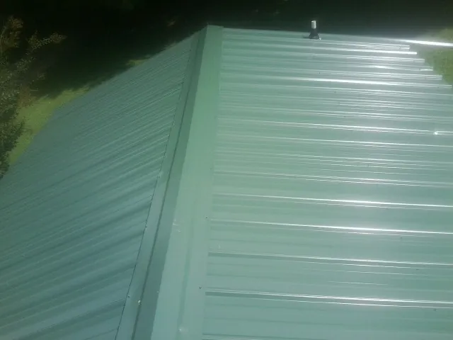 New green metal panels meeting at the ridge of a roof — Flat Roof Repair work by our crew in Gambrills
