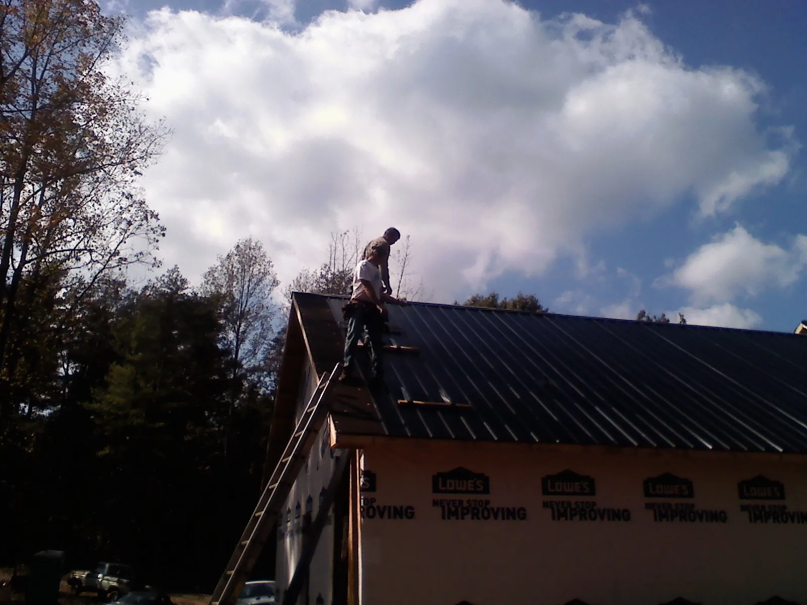 Roofer fastening dark metal panels high against a cloudy sky, from a Roof Inspection job in Gambrills