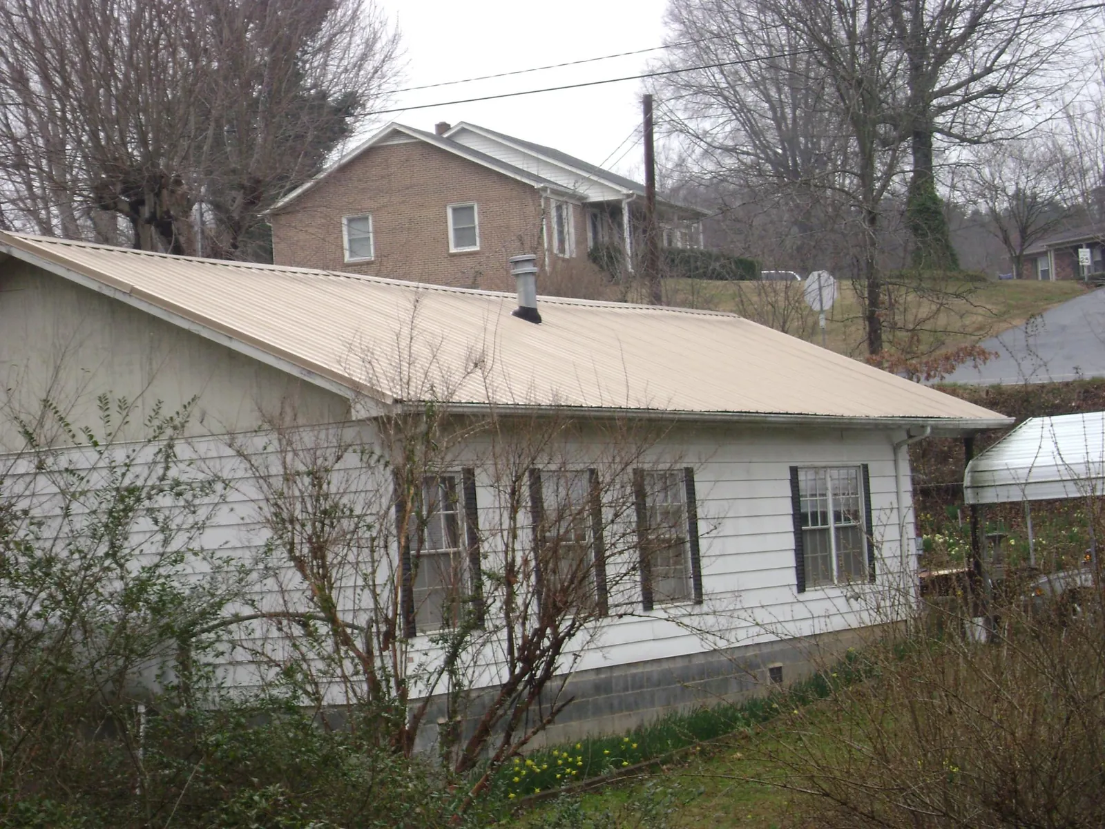 Tan metal roof on a white sided house set into a hillside — Commercial Roofing by Roofing Brothers in Gambrills