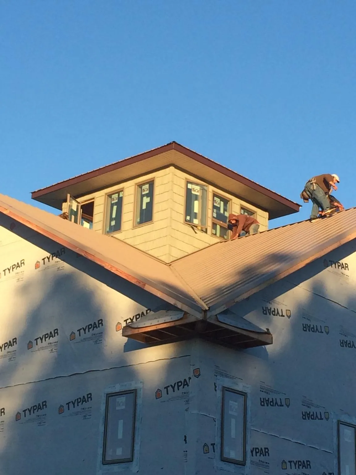 Roofers working around a rooftop cupola on a new metal roof at sunset in Gambrills